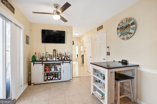 bar featuring light tile patterned floors, baseboards, a dry bar, and a ceiling fan