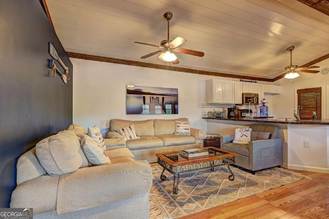 living area with baseboards, ceiling fan, ornamental molding, and light wood-style flooring