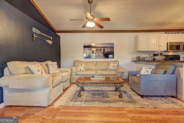 living area with crown molding, a ceiling fan, and light wood-style flooring