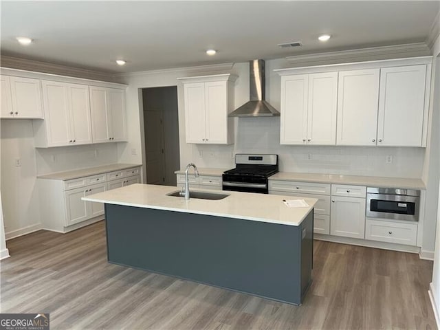 kitchen with a kitchen island with sink, a sink, stainless steel appliances, white cabinets, and wall chimney range hood