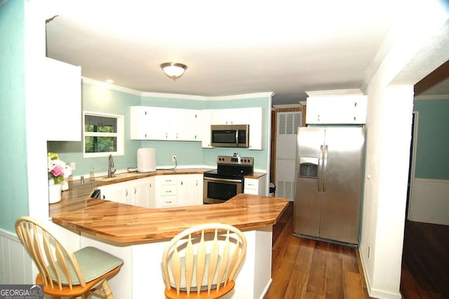 kitchen featuring appliances with stainless steel finishes, a peninsula, crown molding, white cabinets, and wooden counters