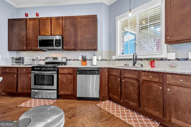 kitchen featuring stainless steel appliances, tasteful backsplash, wood finished floors, and ornamental molding