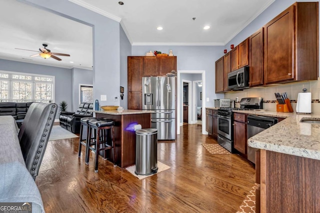 kitchen featuring ceiling fan, open floor plan, a breakfast bar area, appliances with stainless steel finishes, and dark wood-style floors