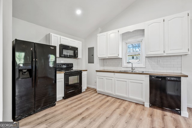 kitchen with light wood finished floors, a sink, black appliances, vaulted ceiling, and white cabinetry