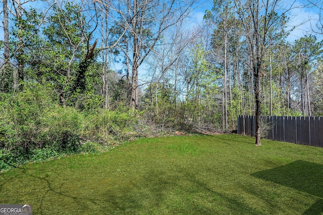 view of yard featuring a wooded view and fence