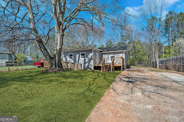 view of front of home with a deck, a front yard, and fence