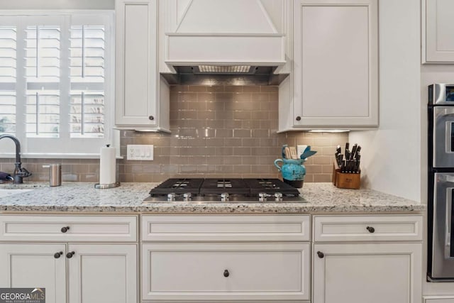 kitchen with decorative backsplash, white cabinets, appliances with stainless steel finishes, and premium range hood