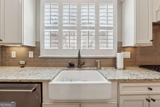 kitchen with stainless steel dishwasher, light stone counters, tasteful backsplash, and a sink