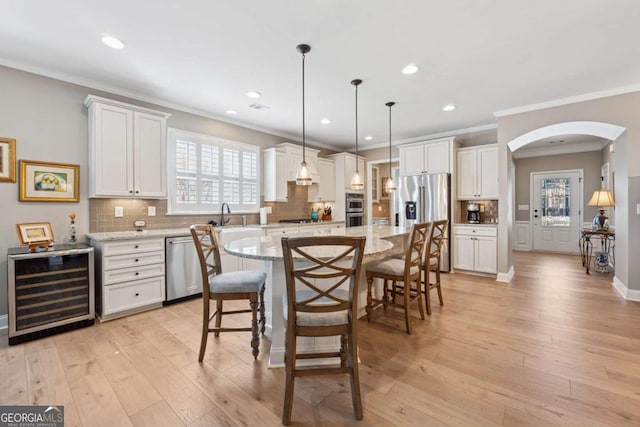 kitchen featuring a breakfast bar, beverage cooler, arched walkways, light wood-style floors, and appliances with stainless steel finishes