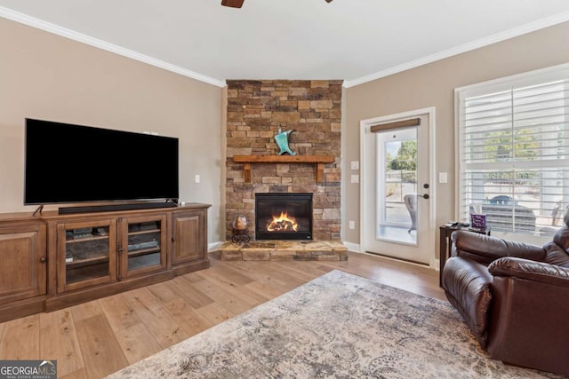 living room featuring light wood-type flooring, a stone fireplace, ceiling fan, and crown molding