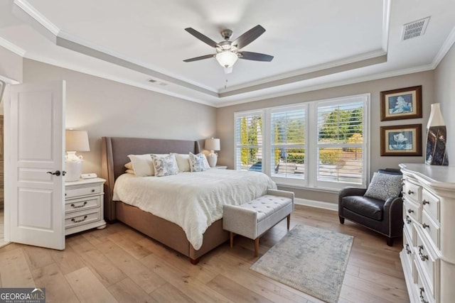 bedroom featuring visible vents, light wood-style floors, a tray ceiling, and ornamental molding