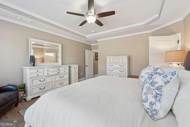 bedroom featuring a ceiling fan, wood finished floors, visible vents, ornamental molding, and a raised ceiling