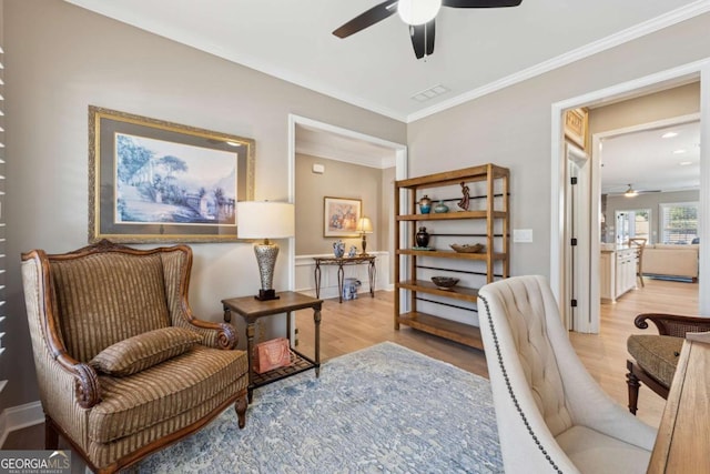 living area featuring light wood finished floors, visible vents, ceiling fan, and ornamental molding