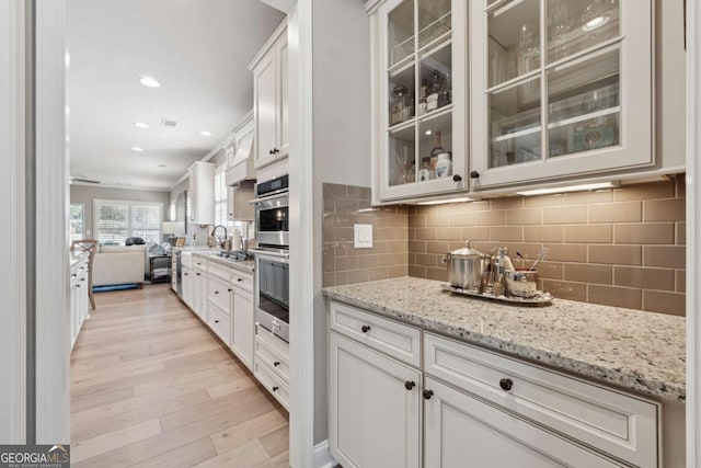 kitchen with light wood finished floors, glass insert cabinets, open floor plan, and backsplash