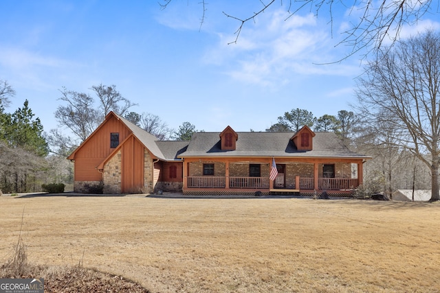 view of front of home with a front yard, covered porch, stone siding, and a shingled roof