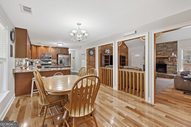 dining area featuring a chandelier, visible vents, a stone fireplace, and light wood-style floors