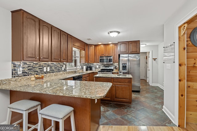 kitchen with a sink, light stone counters, tasteful backsplash, appliances with stainless steel finishes, and a peninsula