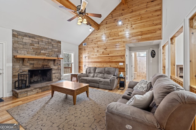 living area featuring wood finished floors, beam ceiling, ceiling fan, a stone fireplace, and wood walls