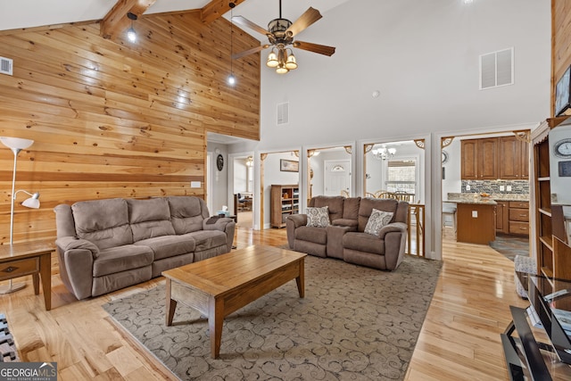 living room featuring light wood-type flooring, visible vents, wood walls, and ceiling fan with notable chandelier