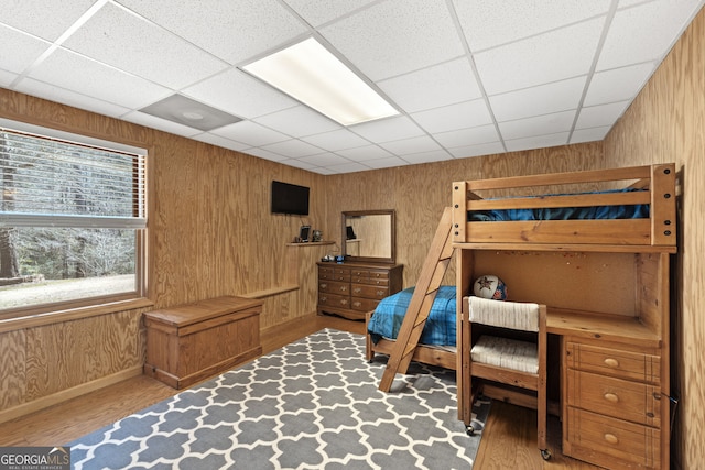 bedroom with wood finished floors, baseboards, wood walls, and a paneled ceiling