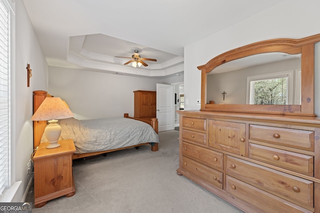 bedroom featuring light colored carpet, a ceiling fan, a tray ceiling, and ornamental molding