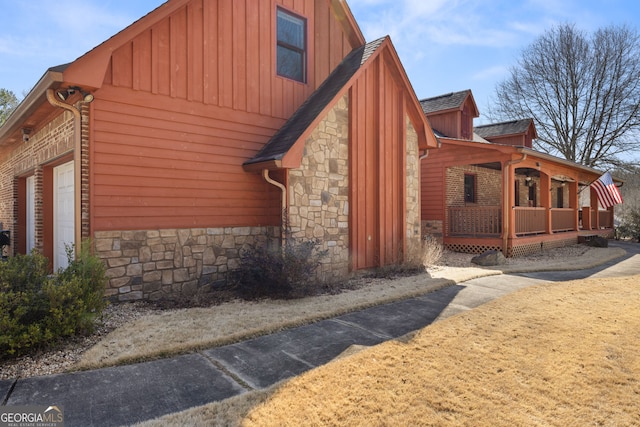 view of side of property with board and batten siding, an attached garage, and stone siding