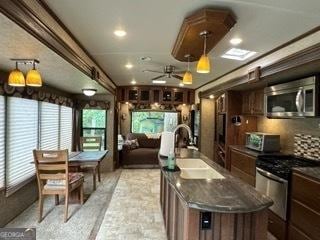 kitchen featuring stainless steel microwave, range with gas cooktop, ceiling fan, a center island with sink, and a sink