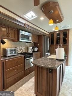 kitchen featuring backsplash, a toaster, appliances with stainless steel finishes, hanging light fixtures, and a kitchen island with sink