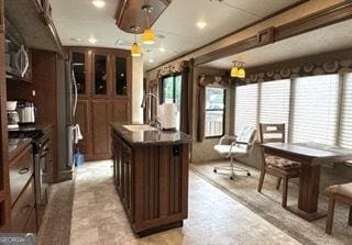 kitchen featuring an island with sink, electric stove, a sink, dark countertops, and dark brown cabinets