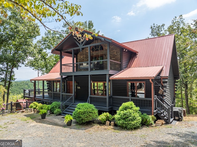 view of front facade with metal roof, stone siding, a balcony, and covered porch