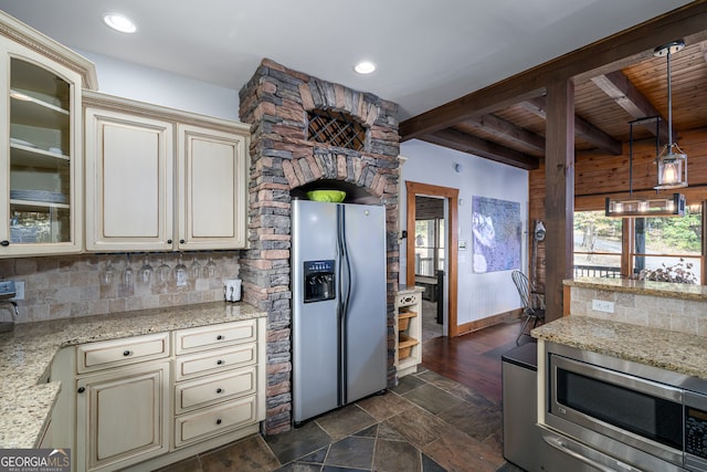 kitchen with beamed ceiling, light stone counters, tasteful backsplash, cream cabinets, and appliances with stainless steel finishes