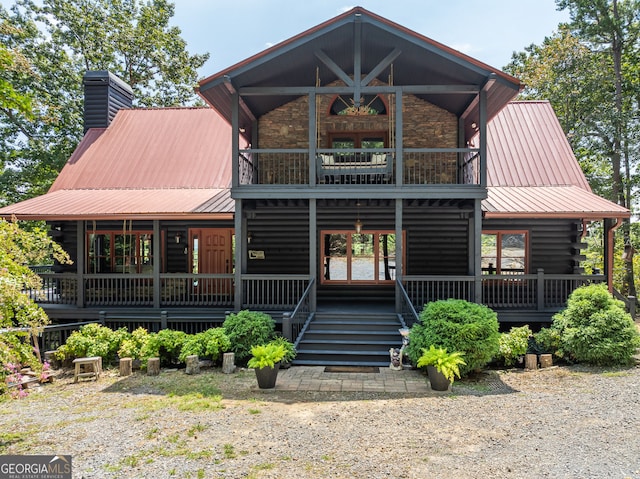 view of front of home with a balcony, covered porch, a chimney, stone siding, and metal roof