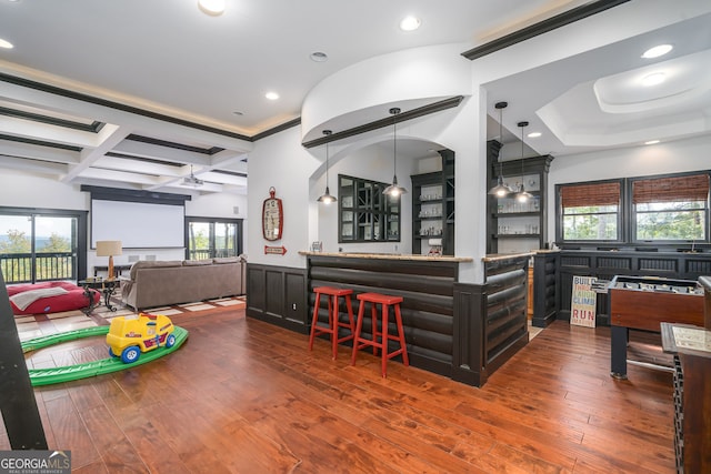 interior space with a wainscoted wall, hardwood / wood-style floors, beam ceiling, a kitchen breakfast bar, and coffered ceiling