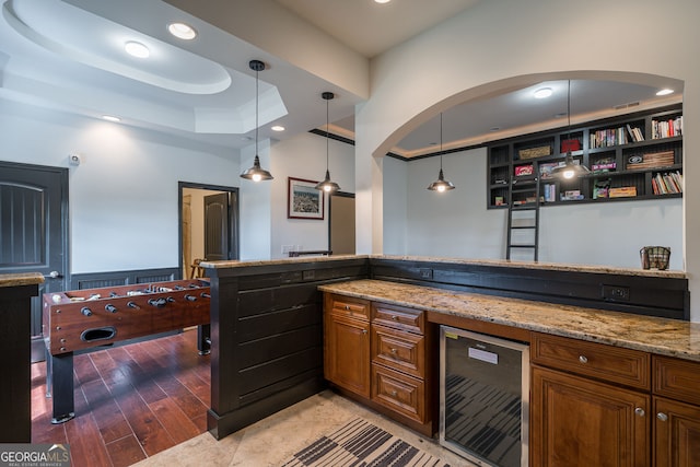 kitchen featuring a tray ceiling, wine cooler, light stone counters, and brown cabinets