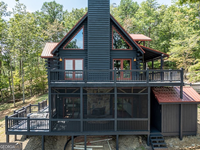 rear view of house with log exterior, a chimney, metal roof, a deck, and a sunroom