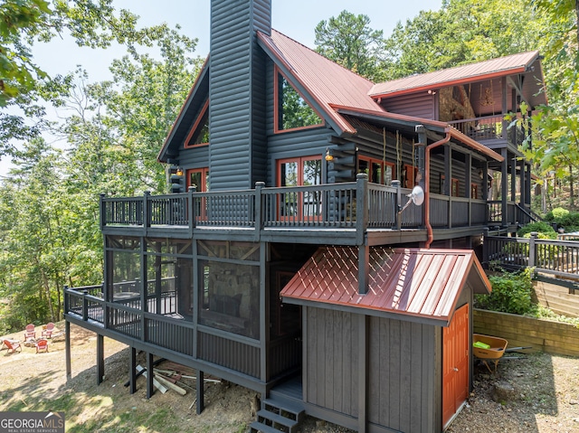 rear view of house with metal roof, a deck, a chimney, and a sunroom