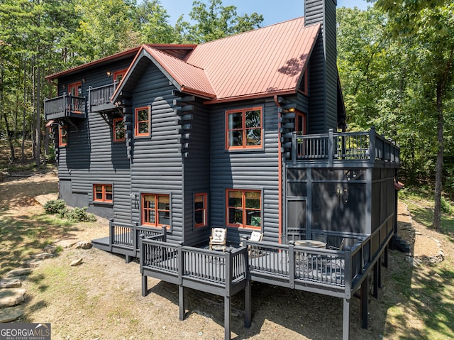 back of property with a chimney, a deck, and metal roof