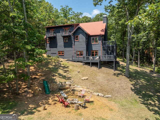 exterior space with an outdoor fire pit, a wooden deck, metal roof, a balcony, and a chimney