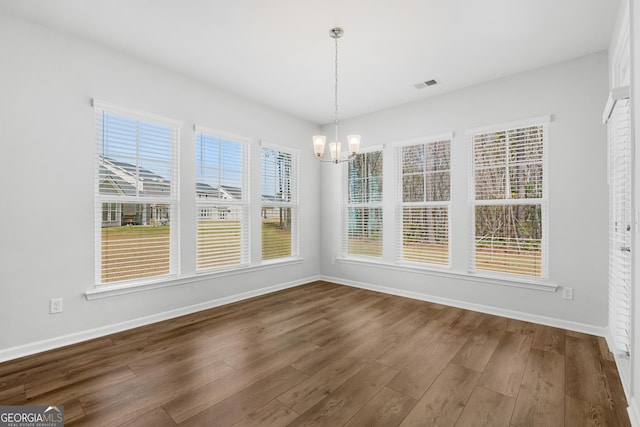 unfurnished dining area featuring an inviting chandelier, baseboards, visible vents, and dark wood-style flooring