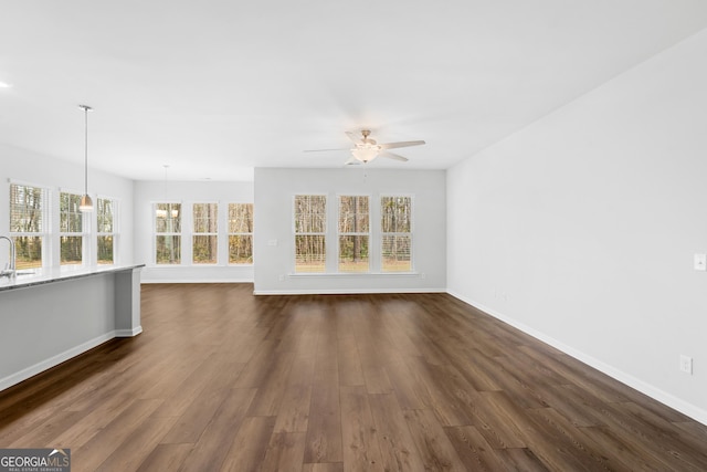 unfurnished living room with dark wood finished floors, baseboards, and a ceiling fan