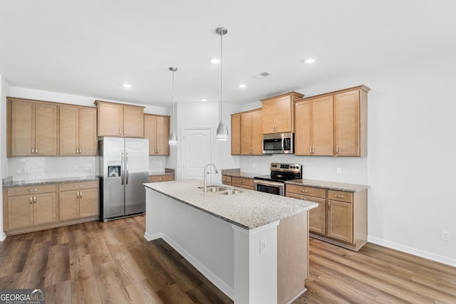 kitchen featuring light stone counters, wood finished floors, a center island with sink, a sink, and stainless steel appliances