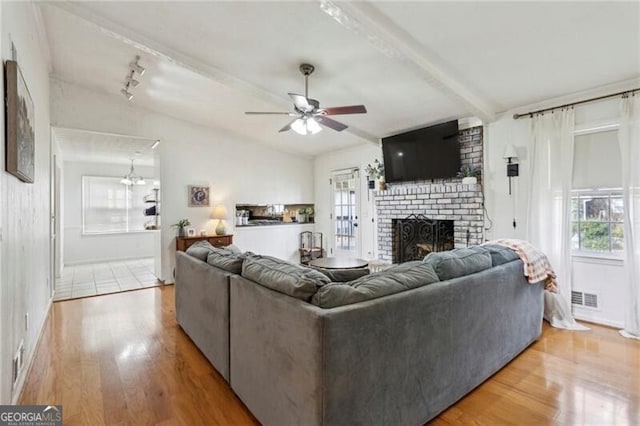 living area with light wood-type flooring, visible vents, a brick fireplace, and vaulted ceiling with beams