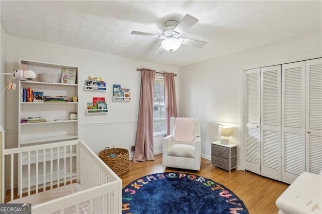 bedroom with a closet, ceiling fan, a nursery area, and wood finished floors