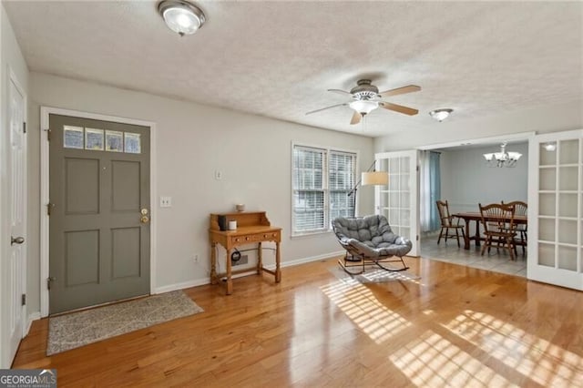 entrance foyer with ceiling fan with notable chandelier, wood finished floors, baseboards, and a textured ceiling