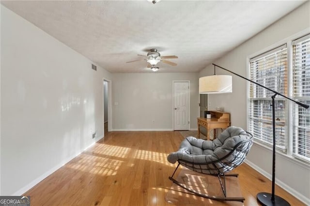 living area with visible vents, baseboards, ceiling fan, wood finished floors, and a textured ceiling