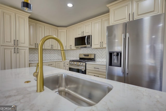 kitchen with light stone counters, a sink, appliances with stainless steel finishes, cream cabinets, and tasteful backsplash