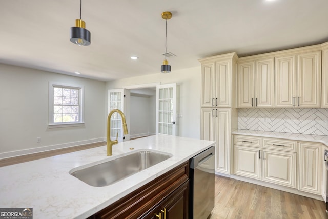 kitchen featuring stainless steel dishwasher, light stone counters, cream cabinetry, and a sink