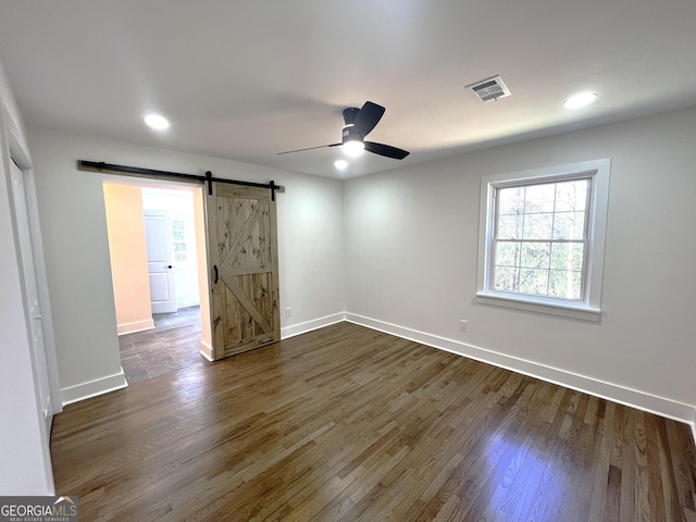 empty room with baseboards, visible vents, dark wood-style flooring, ceiling fan, and a barn door