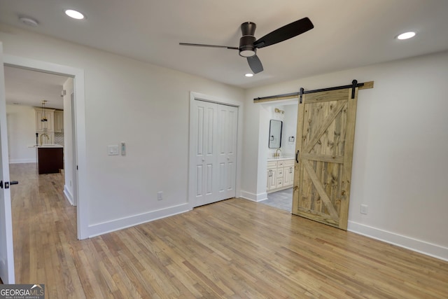 unfurnished bedroom with a barn door, recessed lighting, baseboards, and light wood-type flooring