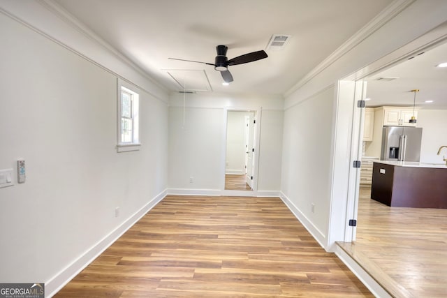 empty room featuring visible vents, attic access, ornamental molding, light wood-style flooring, and a ceiling fan